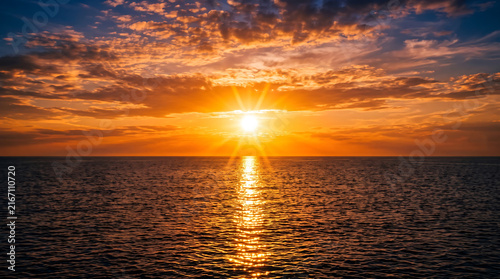 Bright orange sunset over calm ocean water with golden sun rays