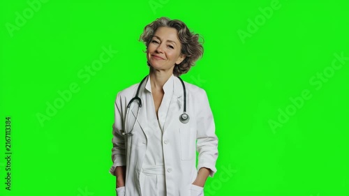 Smiling female doctor wearing a white medical coat and stethoscope standing on green screen background, confident healthcare professional with chroma key copy space