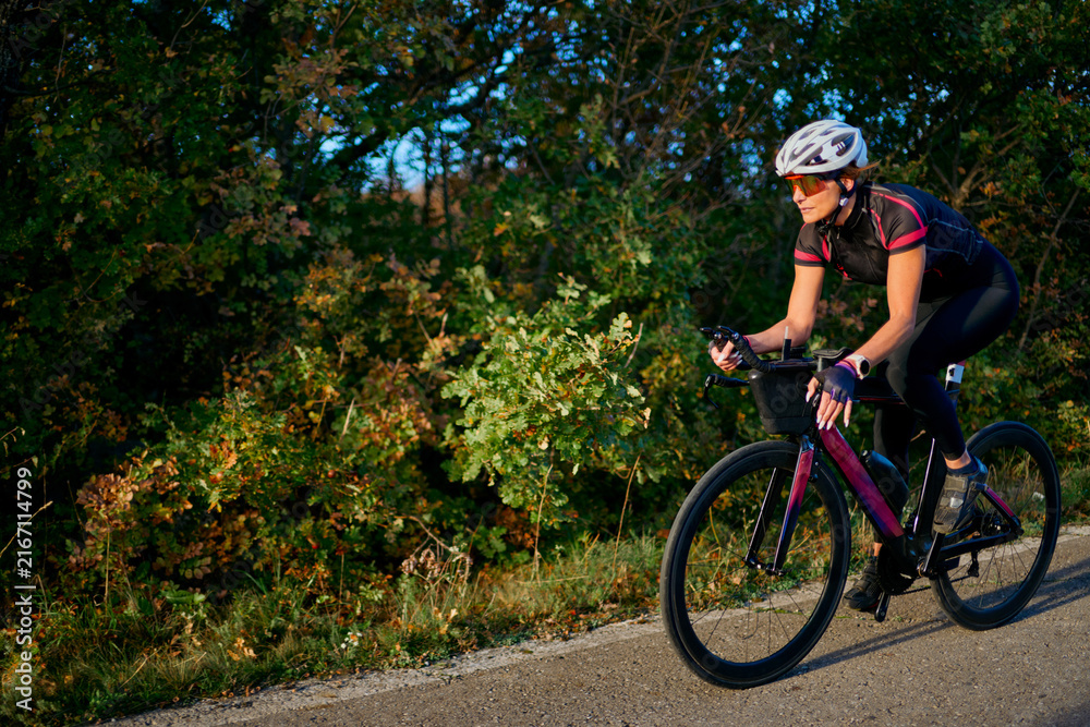Fototapeta premium Female Cyclist Riding Road Bike Along Tree-Lined Country Road During Outdoor Training