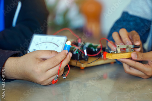 Close up of hands testing an electrical circuit with a multimeter meter and a glowing light bulb.
