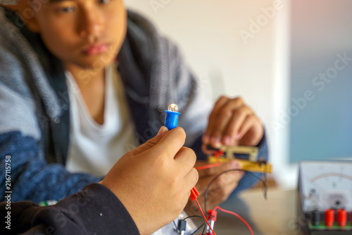 Close-up of a student connecting wires to a glowing small light bulb during a science class experiment.