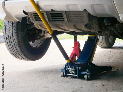 Hydraulic floor jack and red safety jack stand supporting lifted car during underbody maintenance