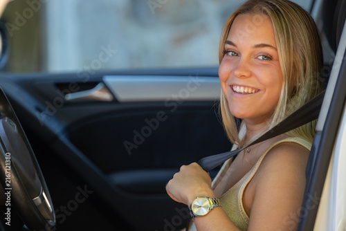 Young smiling woman fastening seatbelt while sitting in car, cheerful female driver ready for safe road trip