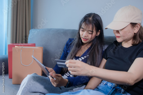 Mother and daughter are shopping online using a tablet while sitting on the sofa at home
