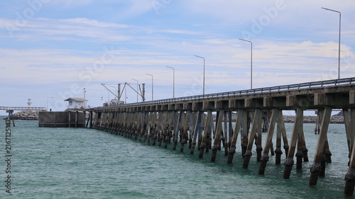 Фотография The image depicts a long pier extending over a body of water, supported by numer