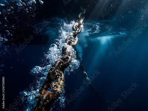 Rusty metal chain sinking into deep blue ocean water with heavy