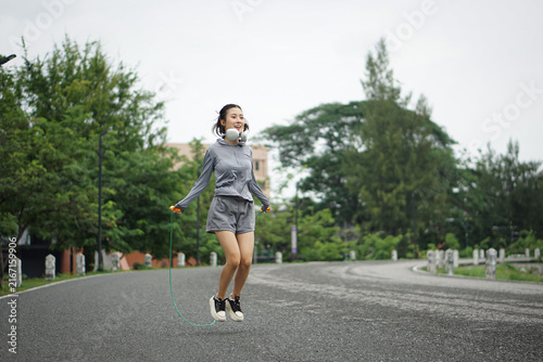 фотографія Action shot of a happy Asian woman captured mid-air while skipping rope on a park road during her morning outdoor workout