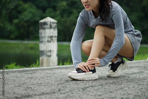 Close-up of an Asian female athlete touching her twisted ankle with a pained expression during an outdoor run.
