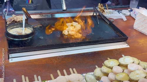 Korean Street Food – Frying Potato Slices with Red Chili Pepper on Hot Griddle at Outdoor Market