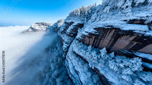 Snow-covered mountain cliffs rising above a sea of clouds under a clear blue sky