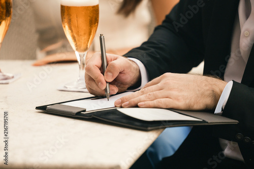 Foto Businessman signs a bill in a leather folder at a restaurant table