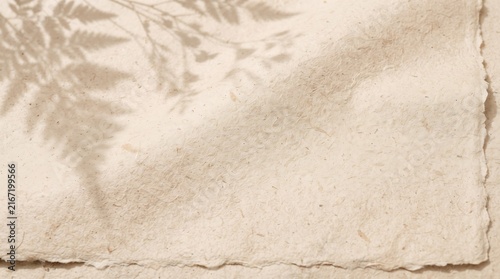 Natural textured beige handmade paper sheet with organic deckle edges and soft fern leaf shadows cast across the rustic grainy surface