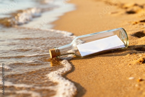 Glass bottle with message lying on sandy beach near gentle waves