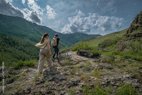 Фотография Rear view of two young women with backpacks hiking on a rocky mountain path over