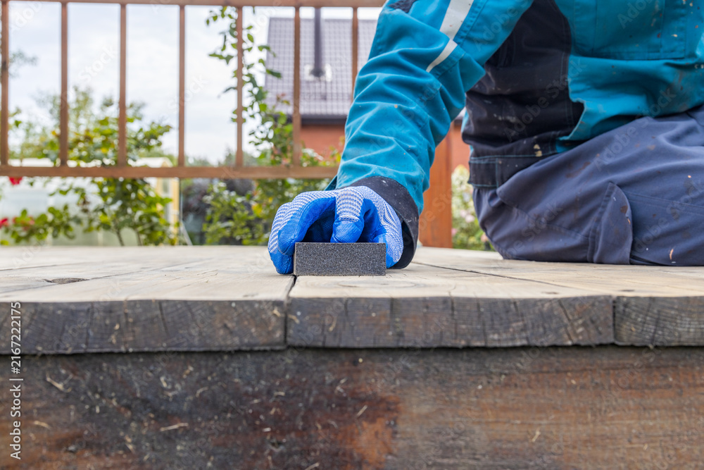 Fototapeta premium Close-up of person cleaning wooden deck with stone abrasive block
