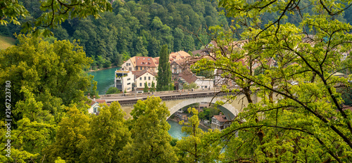 Scenic Panorama of Bern Old Town Bridge and Aare River Framed by Green Tree Leaves in Switzerland on Summer Day