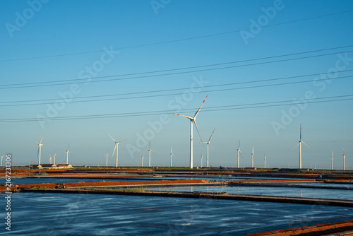 Wind turbines in coastal salt pan area under clear sky