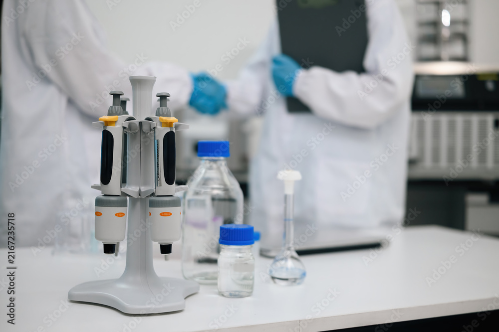 Fototapeta premium Micropipette Stand with Laboratory Glassware on White Bench and Scientist shanking hands in Background