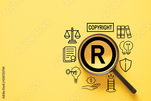 Magnifying glass focusing on a registered trademark R symbol, surrounded by copyright, patent, and legal protection icons on a yellow background. Concept of intellectual property and brand ownership.