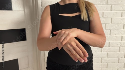 Woman rubbing lotion across hands and forearms indoors, with brick wall background, soft light, skincare routine detail, visible product sheen, clean wellness presentation