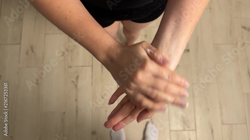 Overhead hands rubbing lotion into skin on light wood floor from personal top-down viewpoint, with hand, lotion, rubbing, application detail, showing skin, palm, finger, wrist context