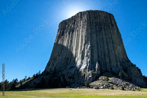 Devils Tower rock formation under clear blue sky with surrounding grassland