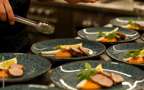 Elegant chef plating gourmet appetizers with tweezers on dark ceramic plates