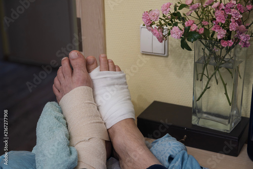 A person has their feet wrapped in medical bandages while resting near a vase of flowers.