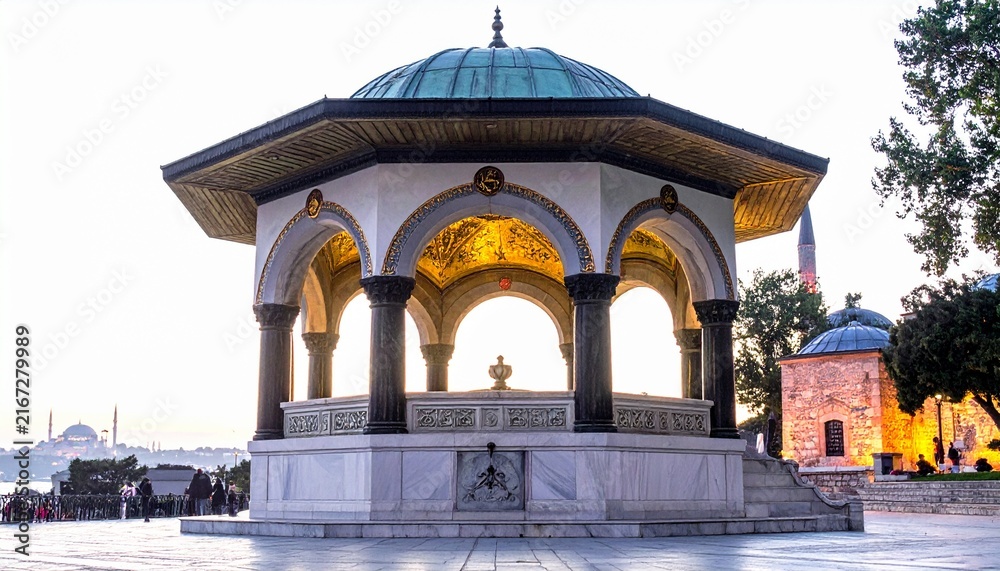 Fototapeta premium A beautifully illuminated historic marble pavilion with ornate arches and a turquoise dome standing proudly in an ancient public square at dusk.