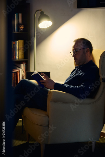 Man reading book in armchair at night