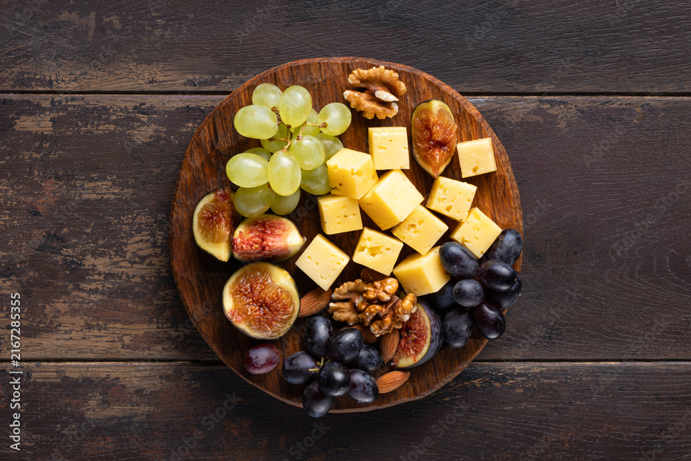 Obraz premium cheese platter with grapes, figs and nuts on wooden background, top view