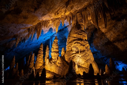 Foto Stalactites and stalagmites in a illuminated cave with reflective water surface
