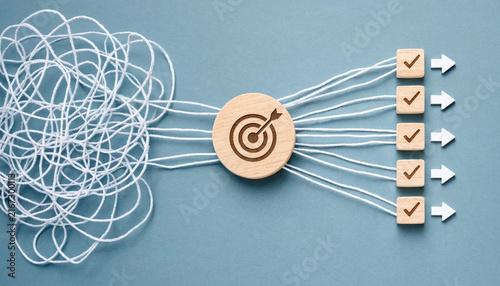 Tangled White Strings Going Through a Round Wooden Target Block and Becoming Straight Lines With Checkmarked Cubes Representing Organizing Chaos Into Clear Business Goals and Actionable Plans