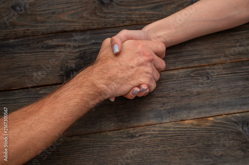 Close up of male and female hands in strong handshake over dark wooden background. Handshake symbolizes partnership, agreement, or support between man and woman. 