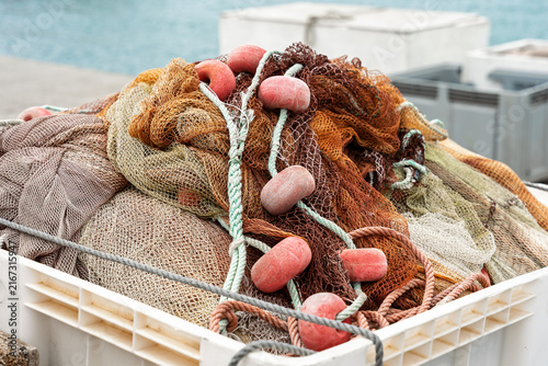 Fishing nets with pink floats and rope coiled in plastic crate at harbor.