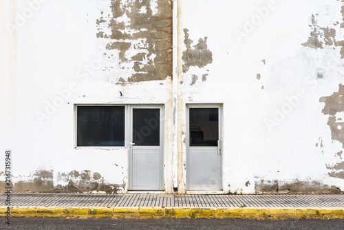 Weathered white wall with two doors and window showing peeling paint texture.