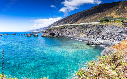 Turquoise ocean cove and dark lava cliffs with banana plantations in La Palma