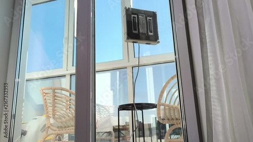 Robot cleaner moves vertically upward on window glass surface. Automated device climbs panel maintaining stable cleaning process. Spring cleaning concept shows efficient smart home