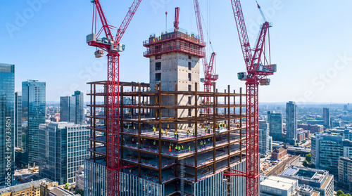 Modern high rise construction site under clear skies with tower cranes with backdrop completed skyscrapers under bright daylight skies