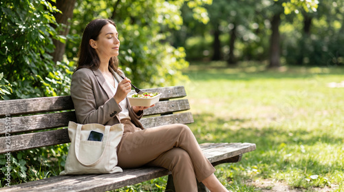Office worker eating lunch outdoors on wooden bench enjoying fresh air and peaceful moment in park