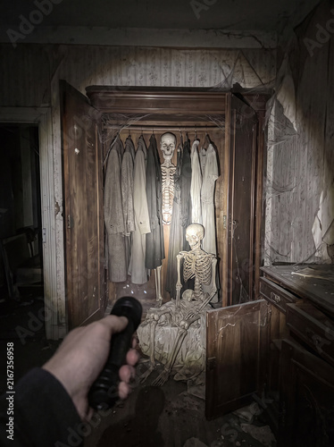 Skeletons in a wardrobe, person with flashlight exploring abandoned building 