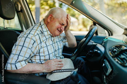 Exhausted senior driver holds his head suffering from sudden medical problems.