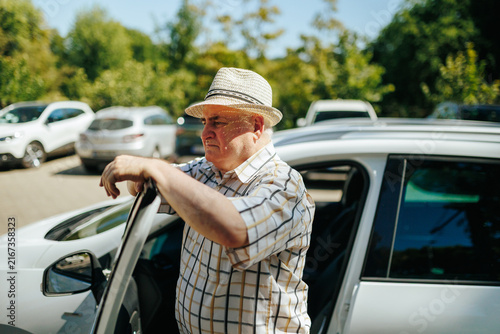 Senior man standing outside the car leaning on the open automobile door.
