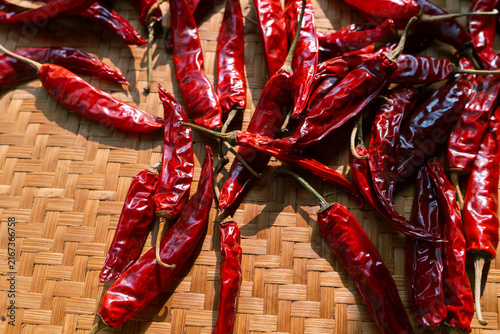 Hand holding dried chili peppers on traditional indonesian woven bamboo basket (besek), prepared to make sambal (spicy sauce), chili oil, or other hot dishes