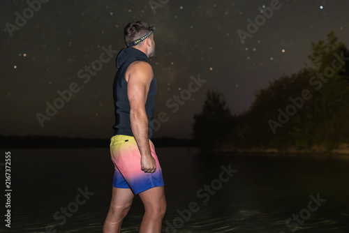 Quadro su tela Man wearing neoprene top standing in lake water under starry night sky