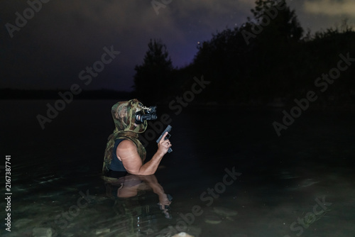 Foto Armed combat diver with night vision holding pistol during night covert mission