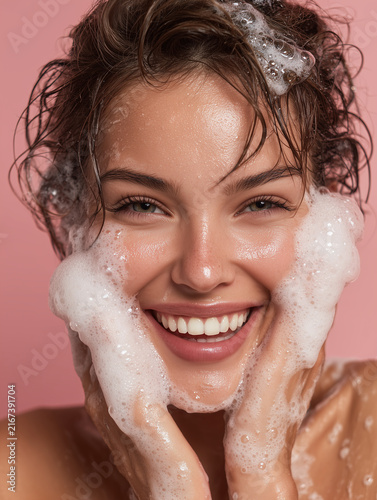 Young woman washing face with foam cleanser smiling