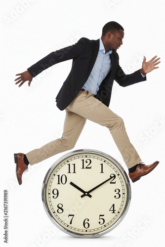Young Businessman Running Over Large Clock Symbolizing Time Management and Deadlines