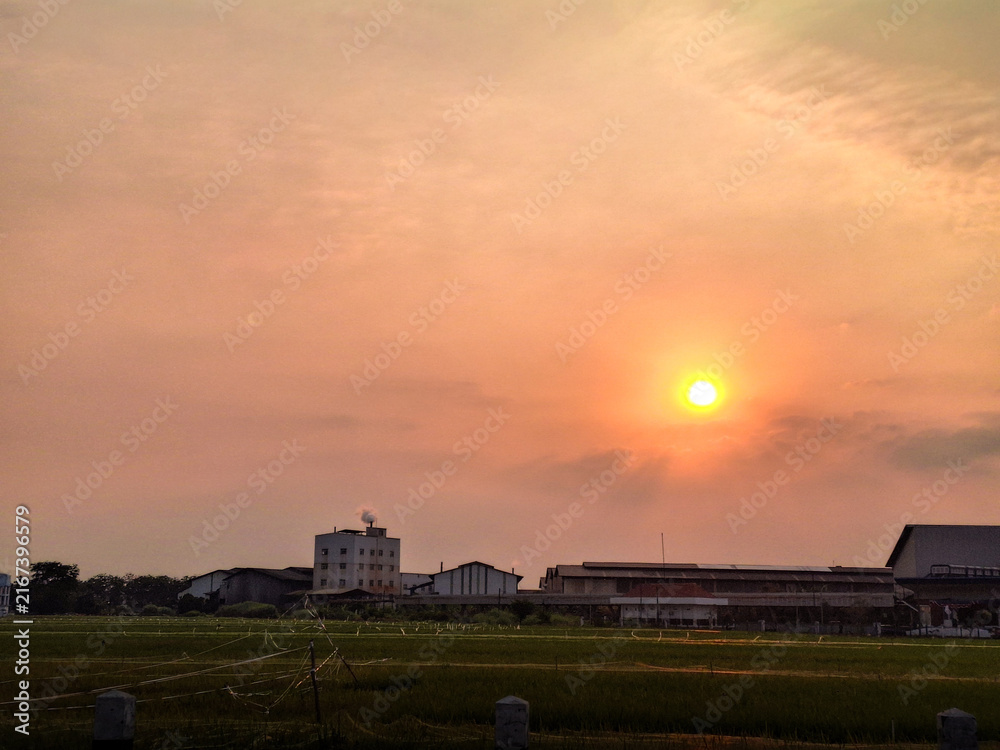 Fototapeta premium Sun sets softly over rural fields and low buildings