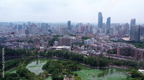An aerial panoramic view of a city combining modern skyscrapers, residential buildings, and a scenic lake with greenery.